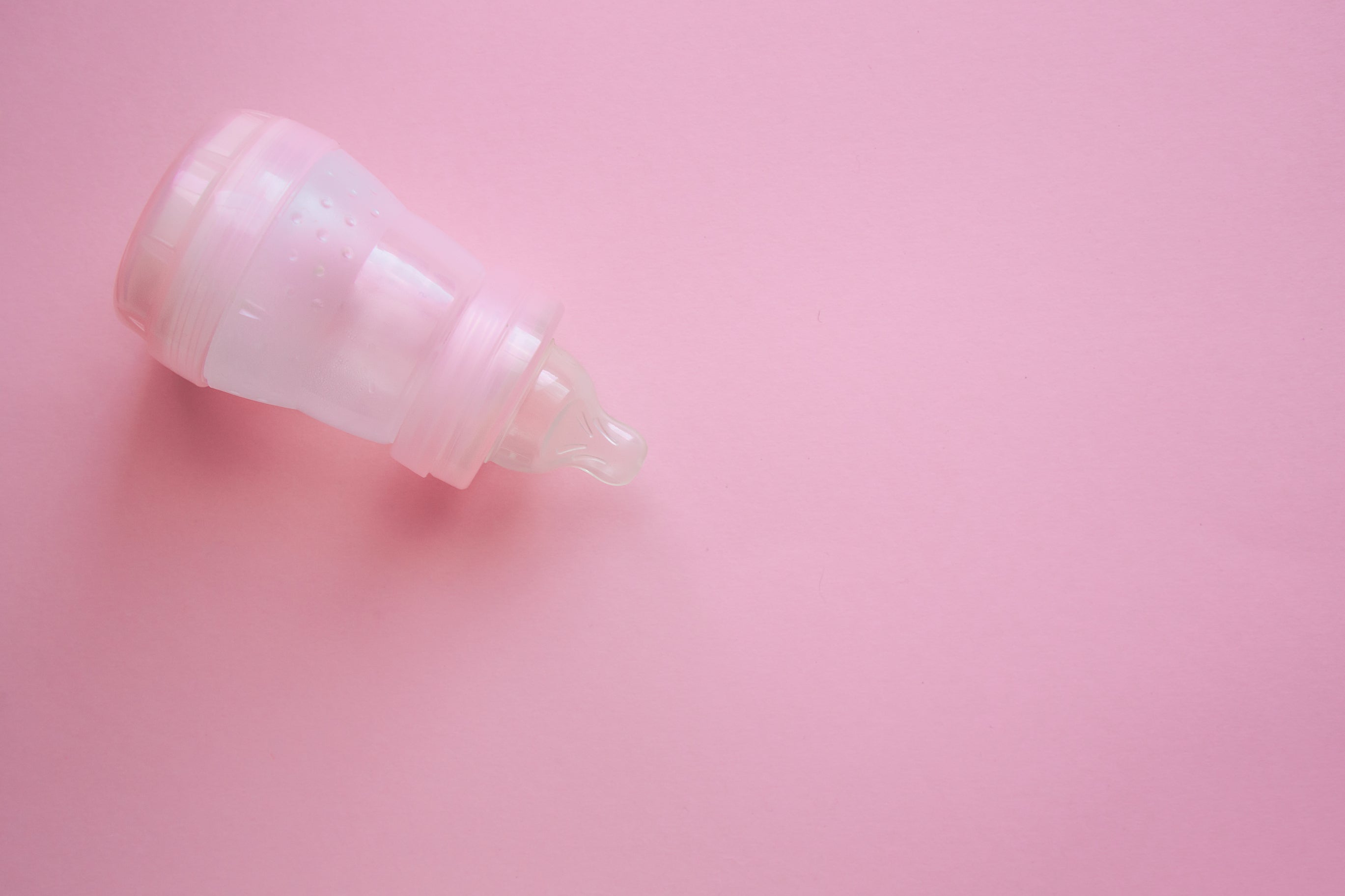 A baby bottle lying on its side against a pink surface. Old baby bottles can be used to store child-friendly paint. This way, you won't have to throw out tons of baby bottles.