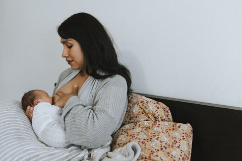 A mother breastfeeds her newborn baby on the bed