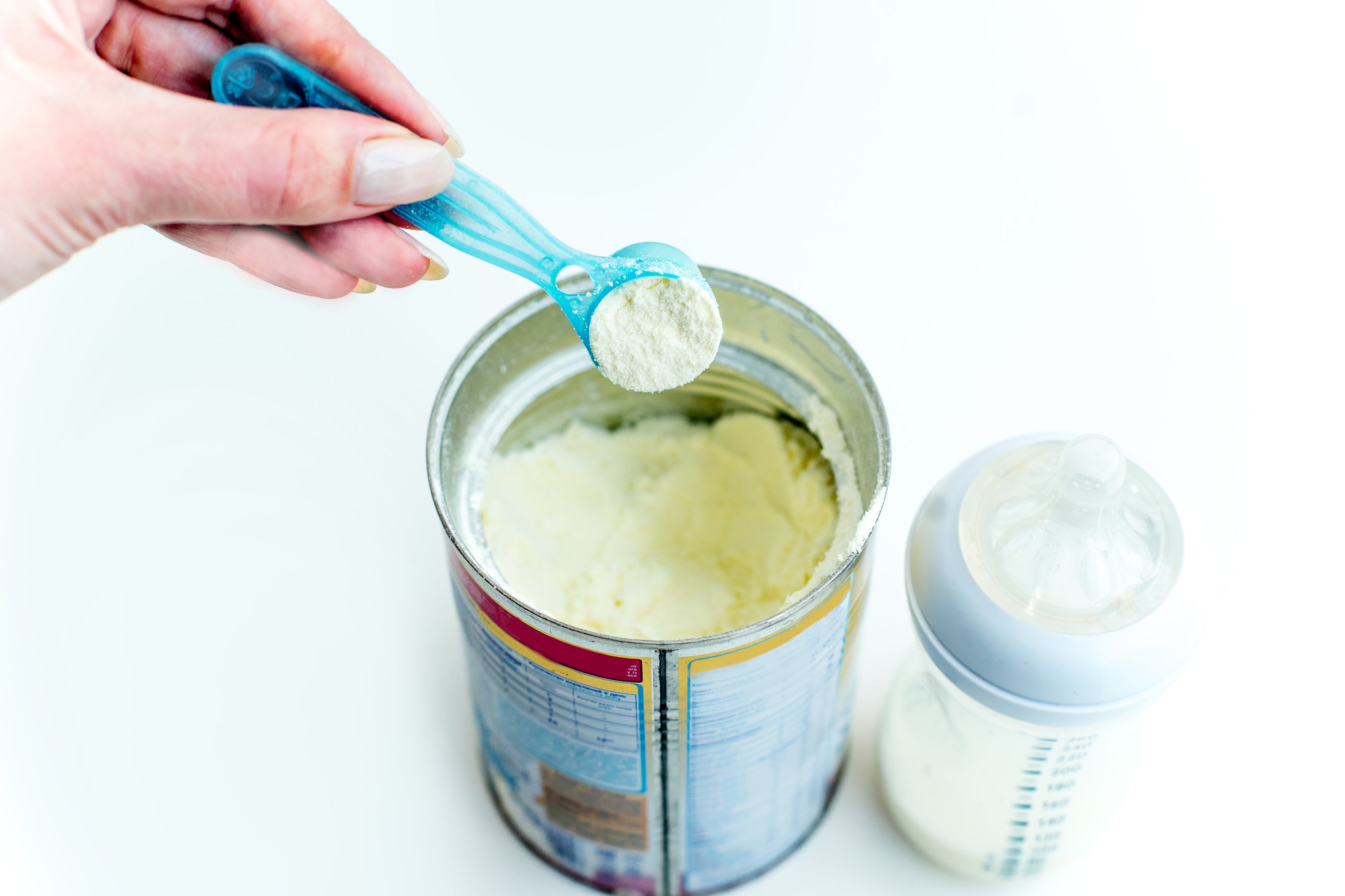 A hand holding a spoonful of baby formula over a can of baby formula and a feeding bottle. Once empty, you can repurpose the baby formula can and turn it into a pen stand, candle holder, or makeup stand!