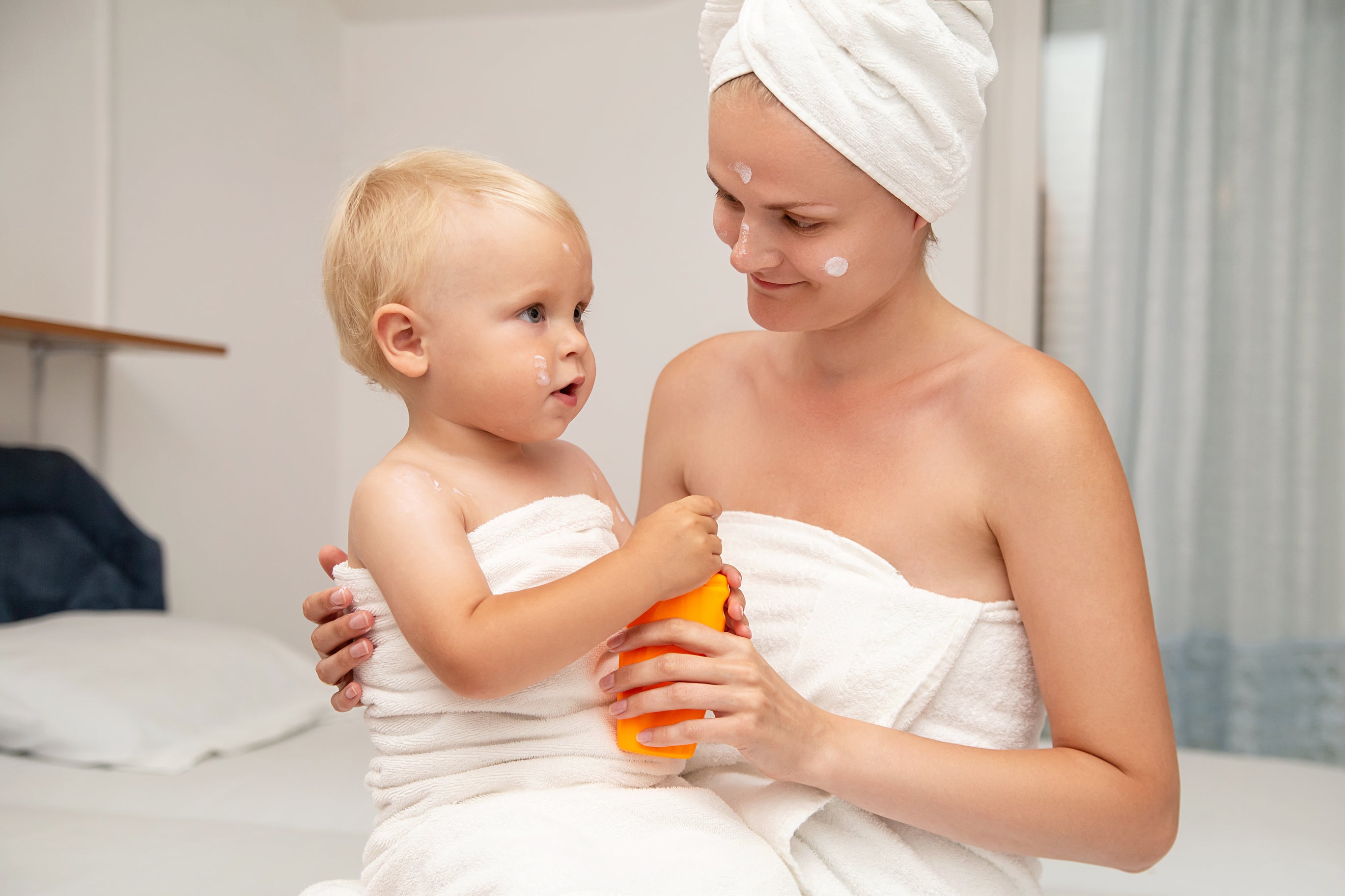 Mother and baby wearing towels and applying baby lotion together. Concept of adult abd baby with sensitive skin using organic baby products.