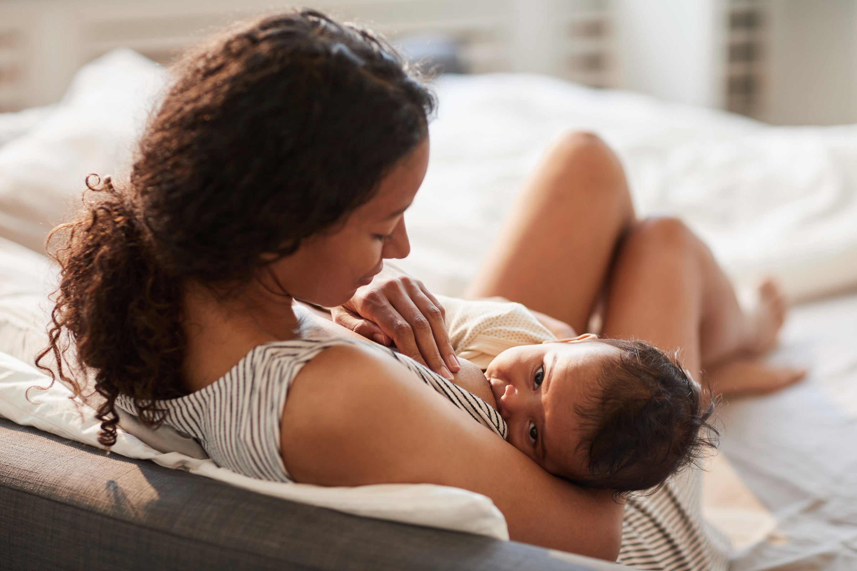 A new mother breastfeeding her baby while sitting on a bed. Concept of breast engorgement, breastfeeding, postpartum.