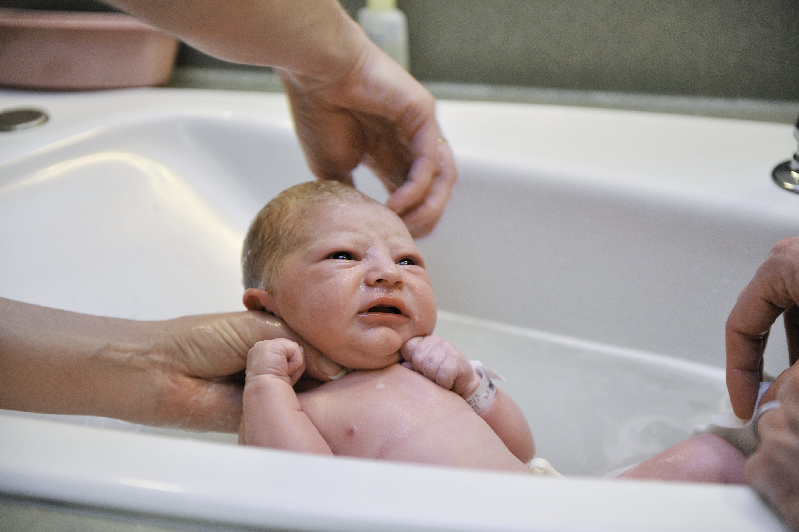 A newborn baby being given a bath 24 hours after birth by a nurse and a parent