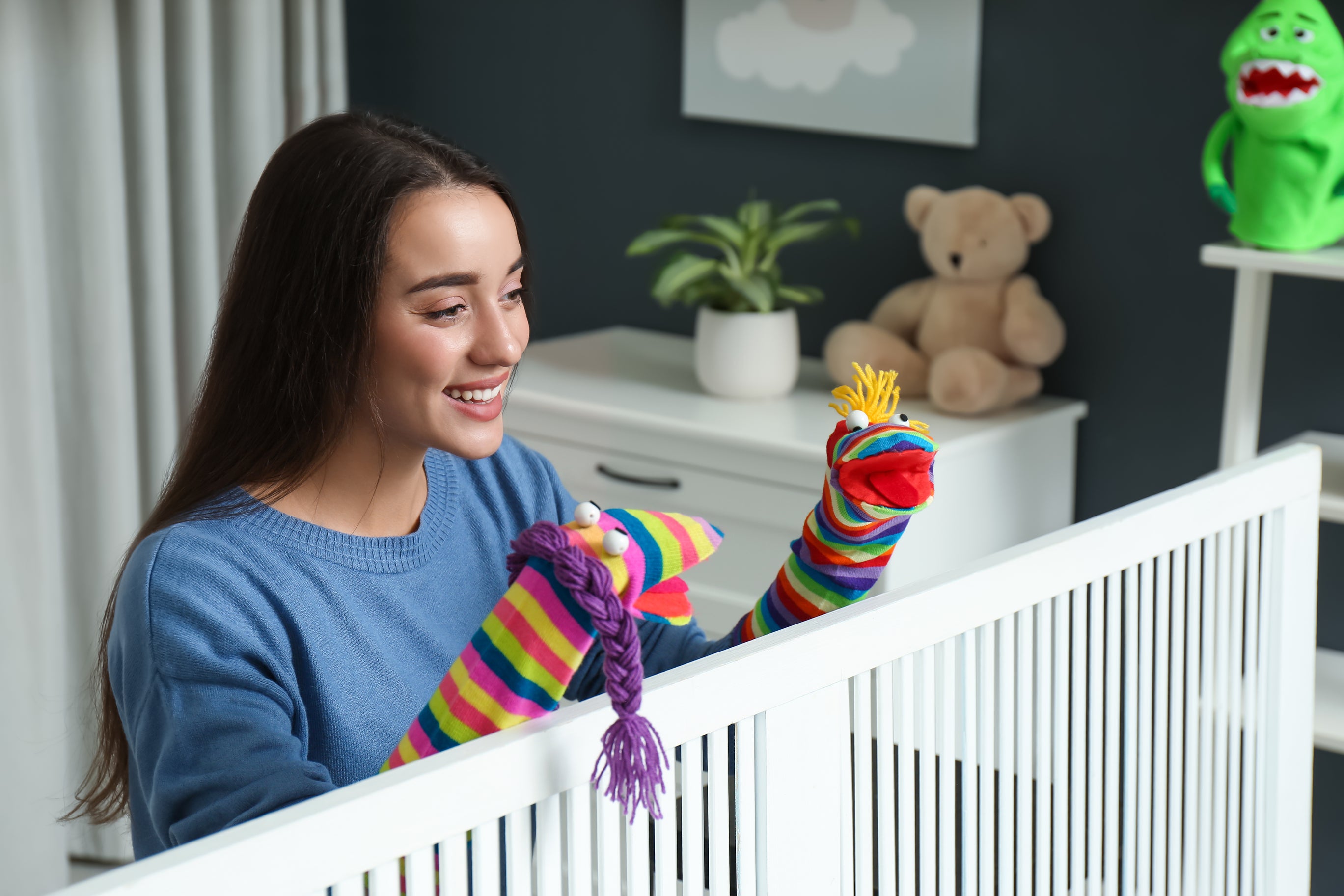 A young mother using DIY sock puppets to entertain her baby in the crib