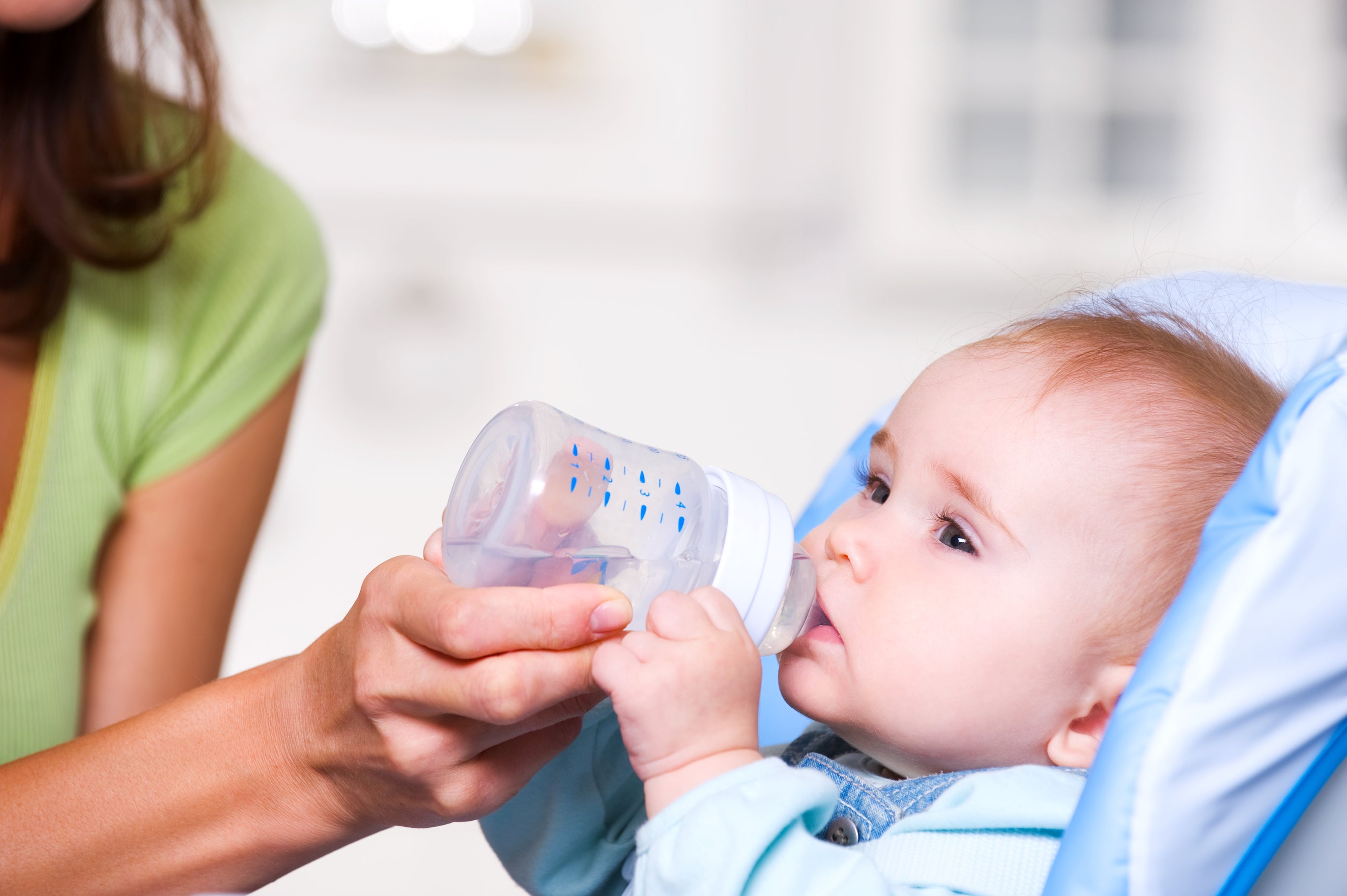 A mother helps her baby drink water from a baby bottle during summer to maintain hydration