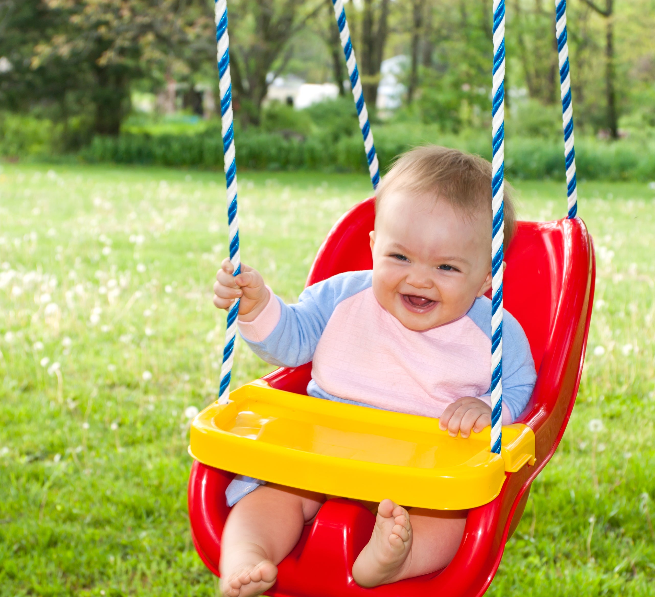 A baby swinging in a baby swing in her front yard. If your child has outgrown their swing, simply replace the seat with a plant pot to repurpose it!