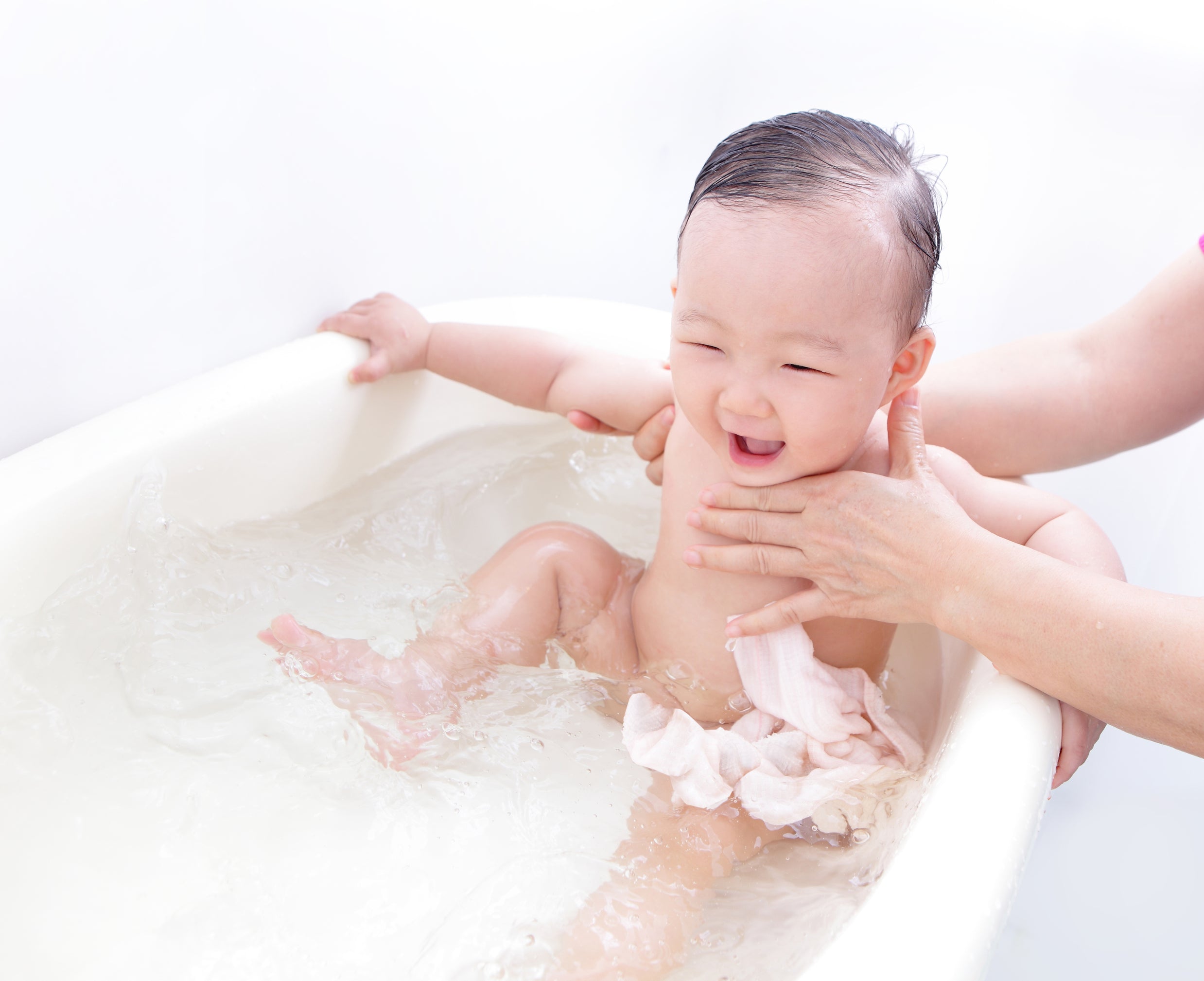 A mother gives a warm bath to her constipated baby who is sitting in a white tub. Warm baths can stimulate bowel movement in babies.