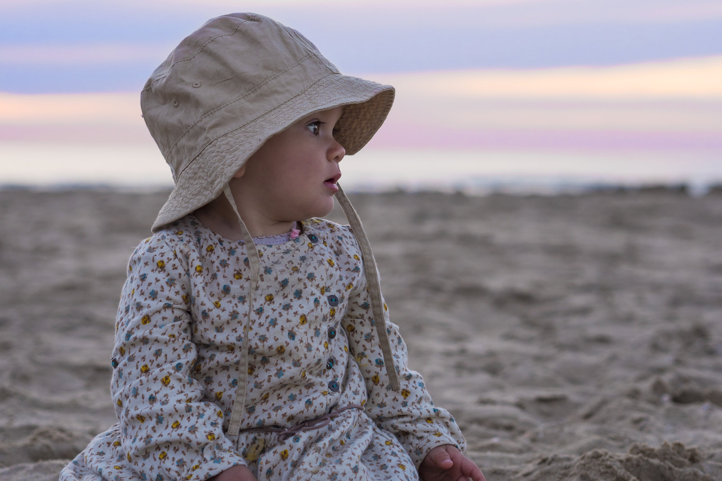 A baby wearing loose cotton clothing and a hat on a beach during summer to stay cool