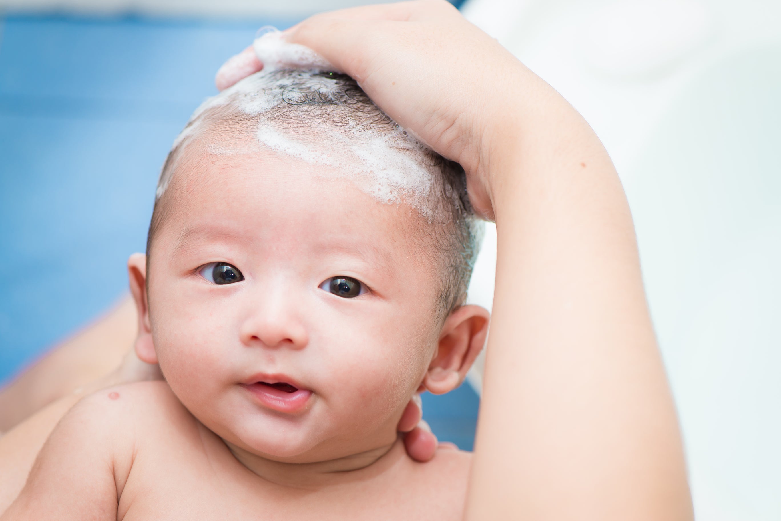 An Asian American baby under six months old being given a bath by the parent