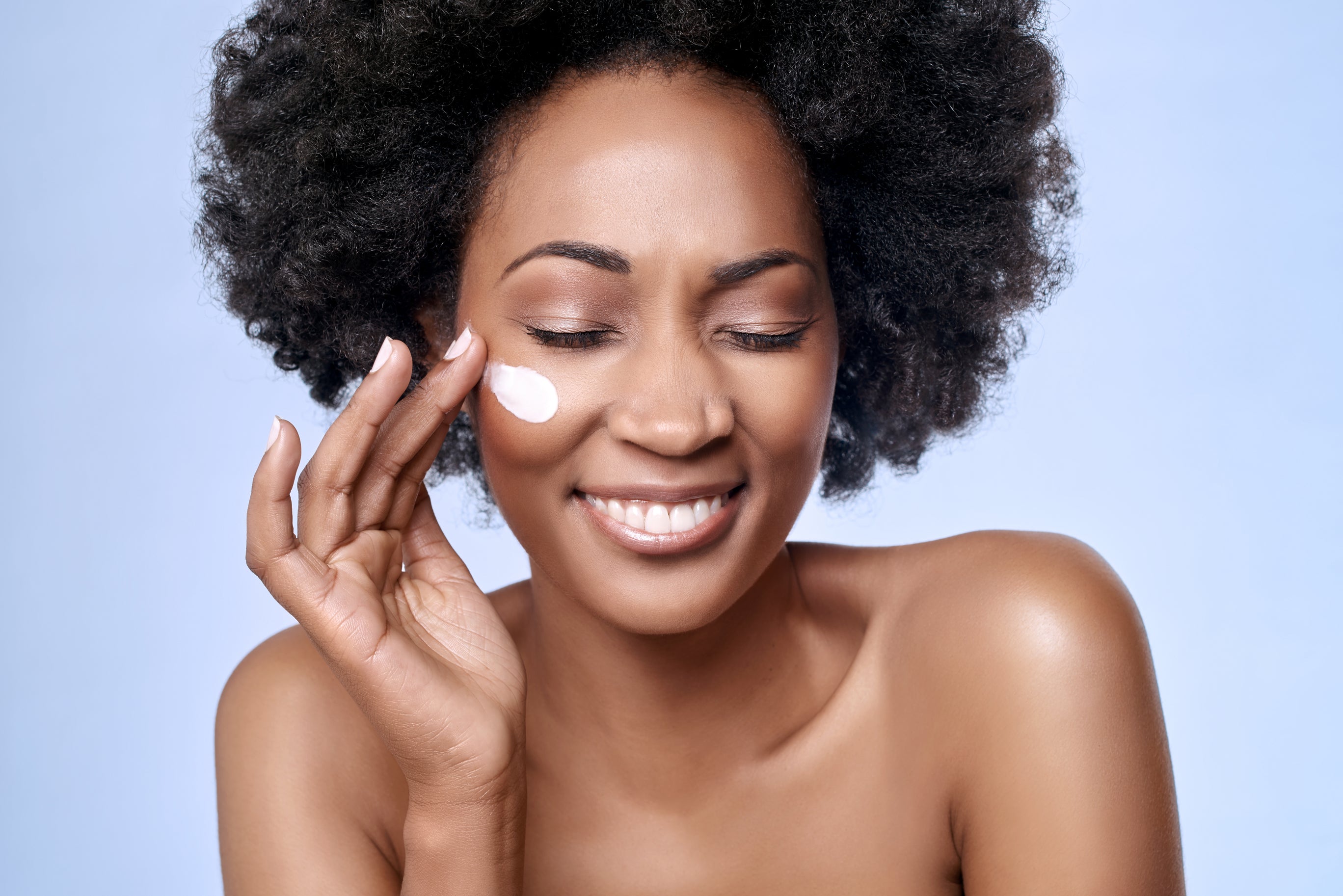 A happy black woman applies baby cream to her face. Concept of adults using baby products. Adults with sensitive skin using baby products.