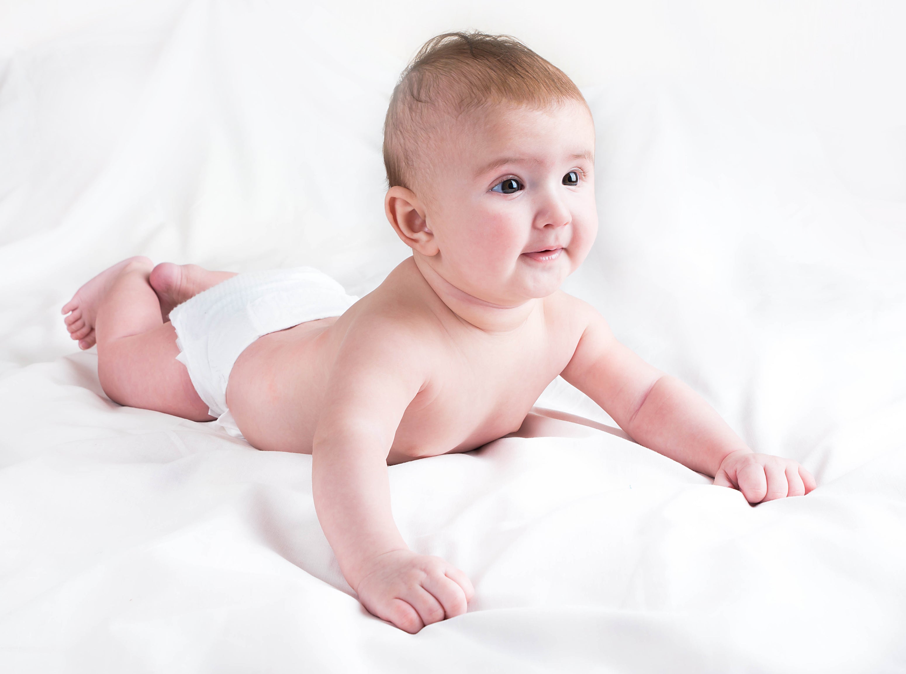 A baby, seen against a white background, wearing just a nappy at home during summers to stay cool and comfortable