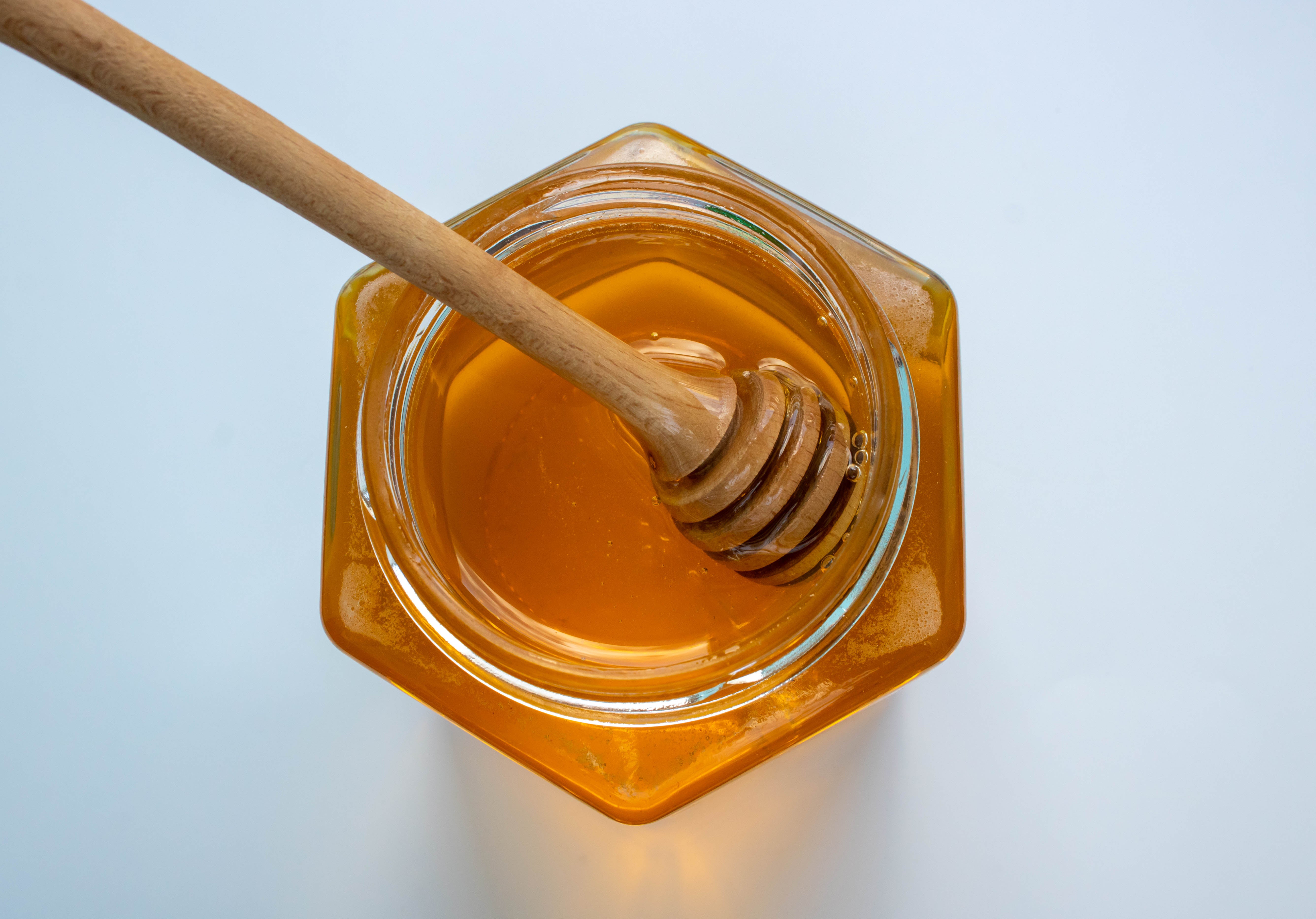 A hexagonal glass jar of honey with a honey dipper. Honey is a popular home remedy for baby cough and cold.