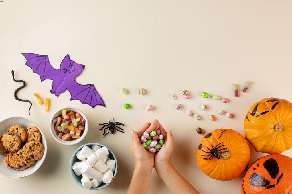 A child holding plastic free and wrapper less Halloween candy on a table. Donuts, pumpkins, cookies, marshmallows, and toffees visible.
