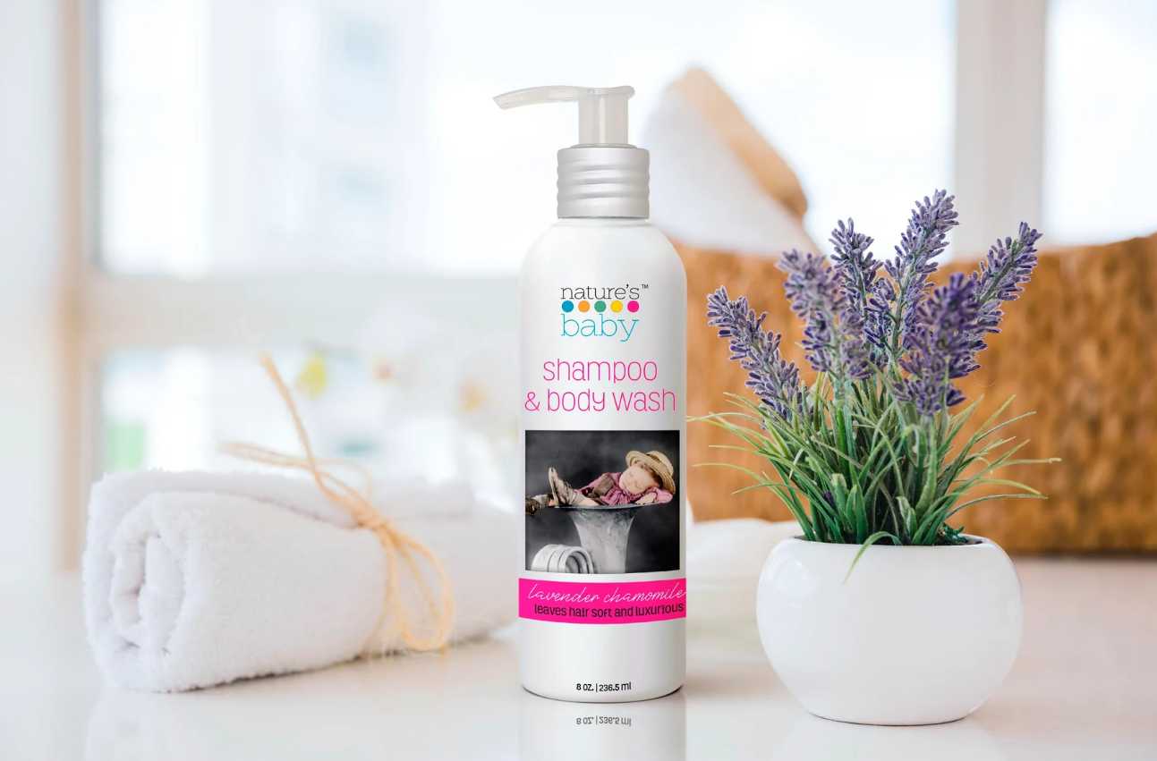Nature's Baby Organics Shampoo & Body Wash Lavender Chamomile bottle on a table along with a plant and a towel. Baby shampoo and baby body wash can be used by grownups as well.