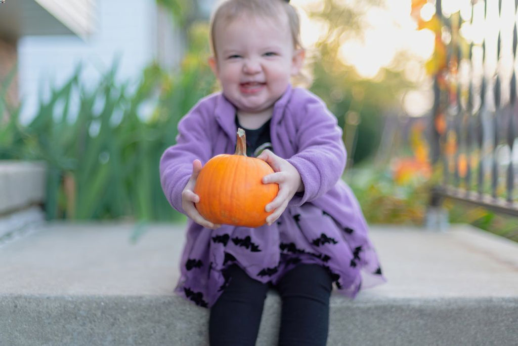 A toddler girl holds a pumpkin during Halloween. 