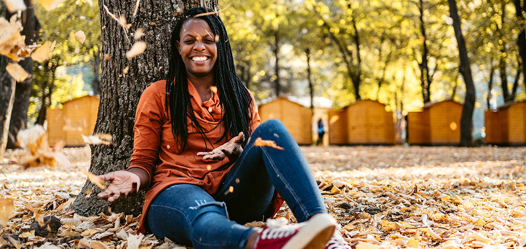 African-American woman sitting on a ground in a public park throwing autumn leaves