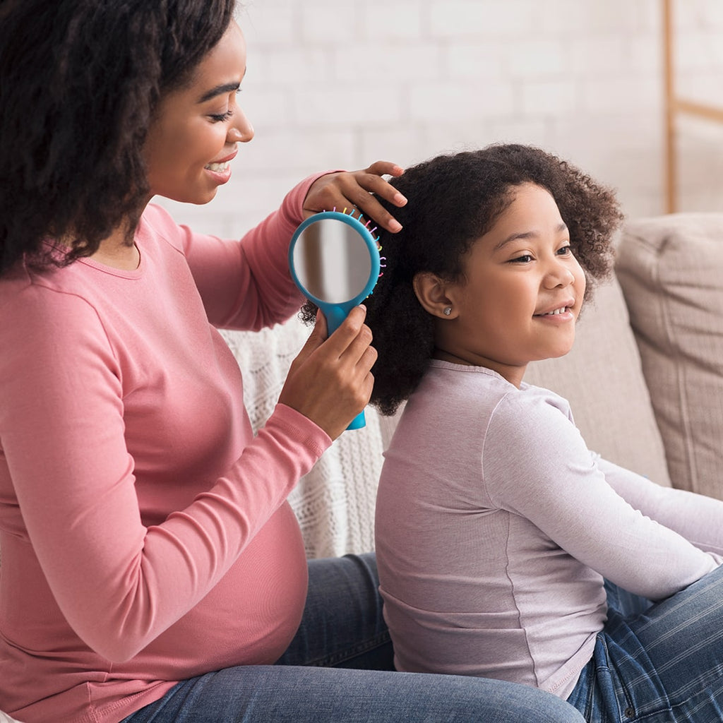 Pregnant woman brushing little black girls hair