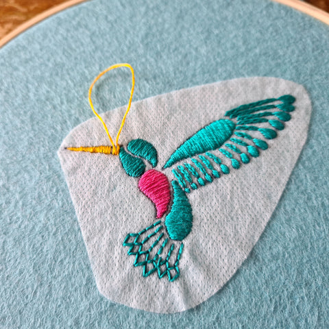 a close up of a hand embroidered turquoise hummingbird, stitched onto turquoise green felt with transfer paper