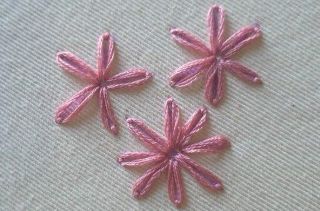 Three embroidered Lazy Daisy stitches in pink thread on white fabric background