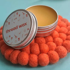 an open tin of beeswax sits on top of a bright orange coaster