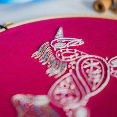 A close up of a unicorn design embroidered in white thread on a bright pink background