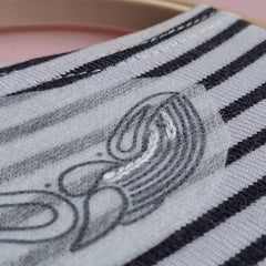 A close up of a stripy shirt in an embroidery hoop. A piece of translucent paper with a whale design is stuck near the neckline; and a row of embroidery stitches is on the whale's belly