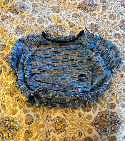 The top of a half finished sweater out of blue and gray variegated yarn