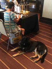 Kelly sitting trying out pens while a GSD named Bailey lies down beside.