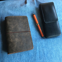 A leather notebook cover, a leather pen case, and a small orange vintage pen.