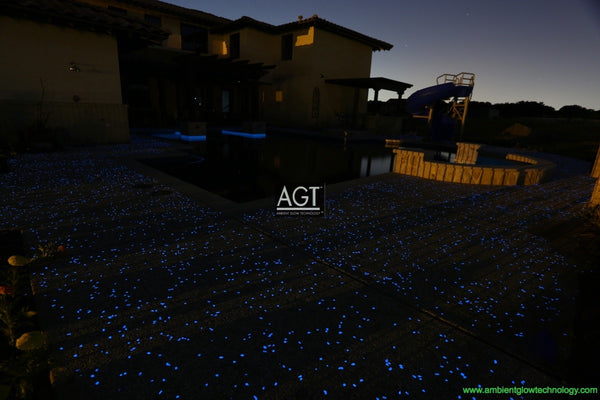 Night time view of a glowing concrete pool deck in Texas, powered by 1/2" AGT Commercial-Grade Glow Stones in Sky Blue with accents of 1/2" Aqua Blue glow rocks.