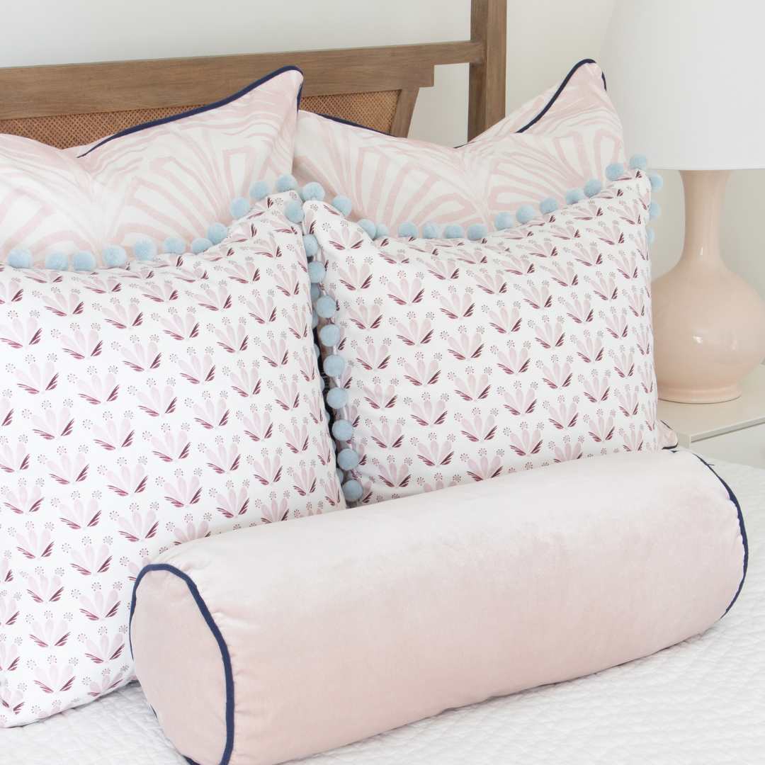 Rose pink palm custom pillows, pink and burgundy drop repeat floral custom pillows and light pink velvet custom pillow styled on a light wood bed with white sheets.