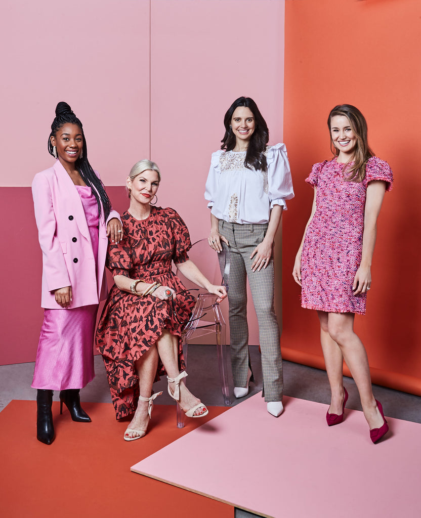 four woman posing in front of a pink and red background