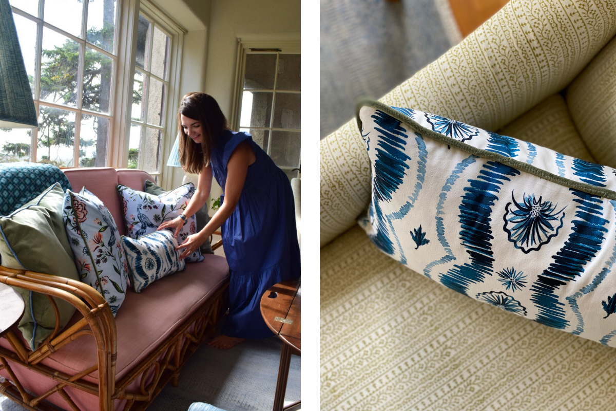 Pink Couch styled with two fern green velvet custom pillow, two Daphne powder custom pillows, and one Blue Ikat custom lumbar pillow in front of brunette woman wearing a blue dress bending down touching Blue Ikat custom lumbar pillow