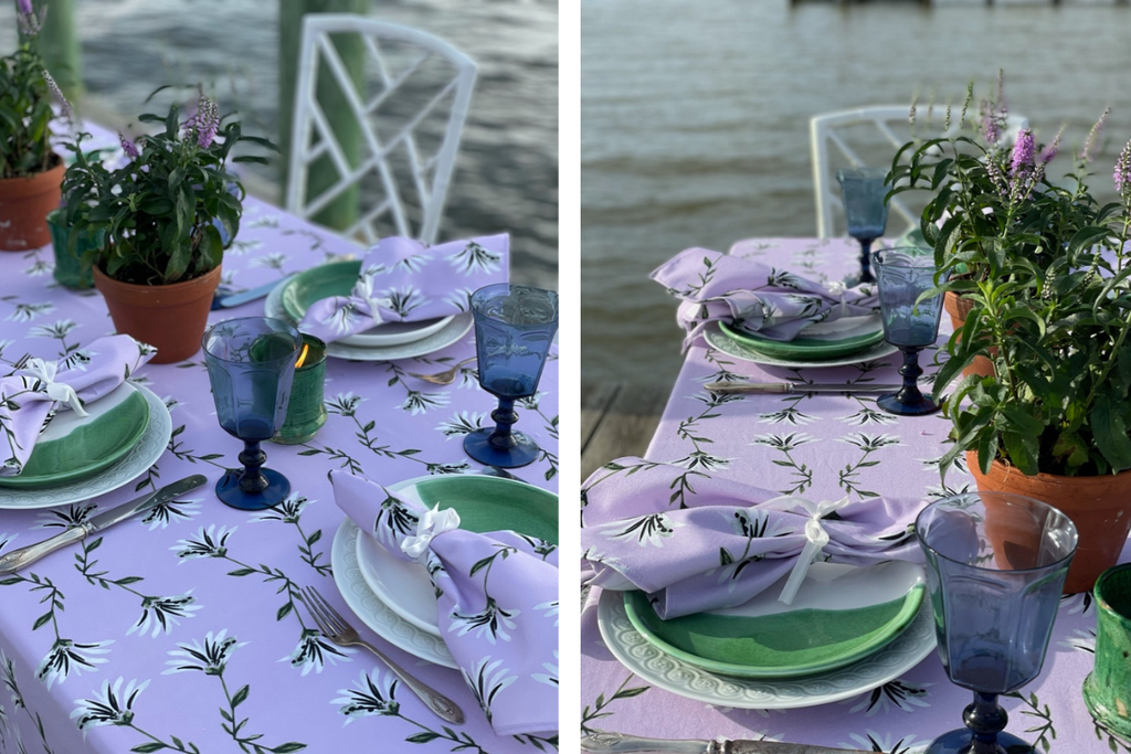 Close up of lavender floral tablecloth and lavender floral napkins styled with green and white plates and blue glasses