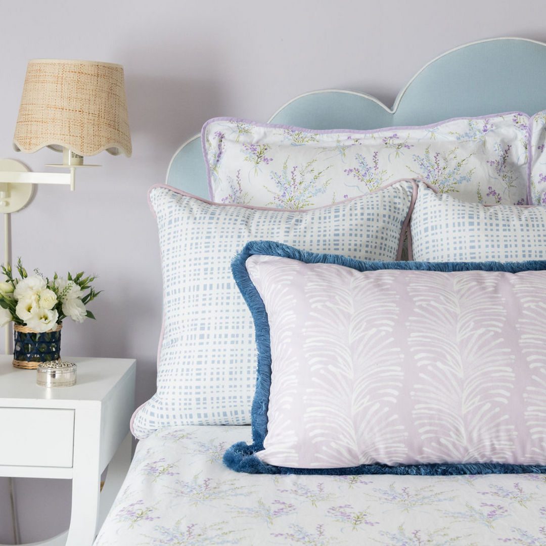 Bed close-up styled with two white floral printed pillows, two Plaid Sky Blue custom pillows, and one Lavender Botanical Stripe custom lumbar pillow