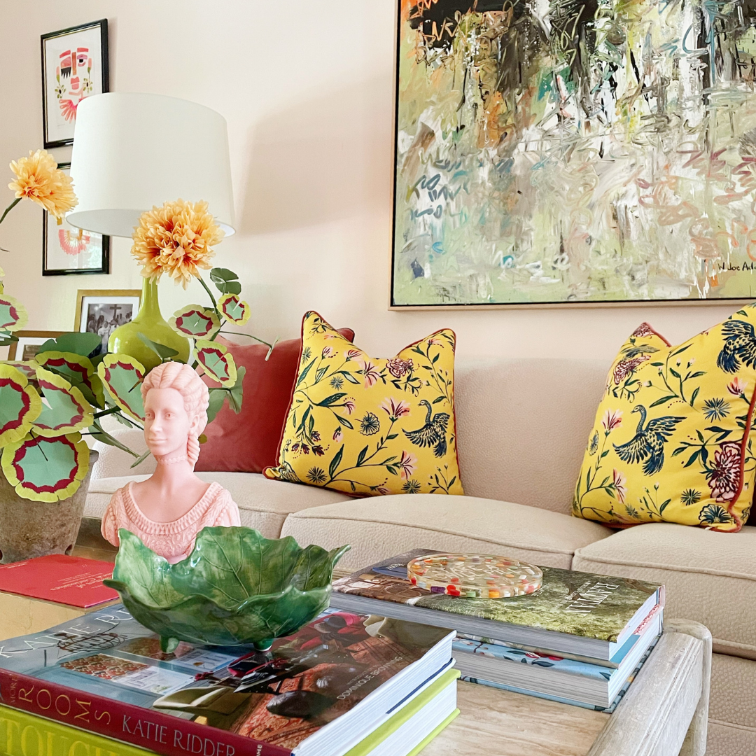 Living room styled with a white couch with a coral velvet custom pillow and two yellow chinoiserie custom pillows next to a coffee table with decorations and a plant