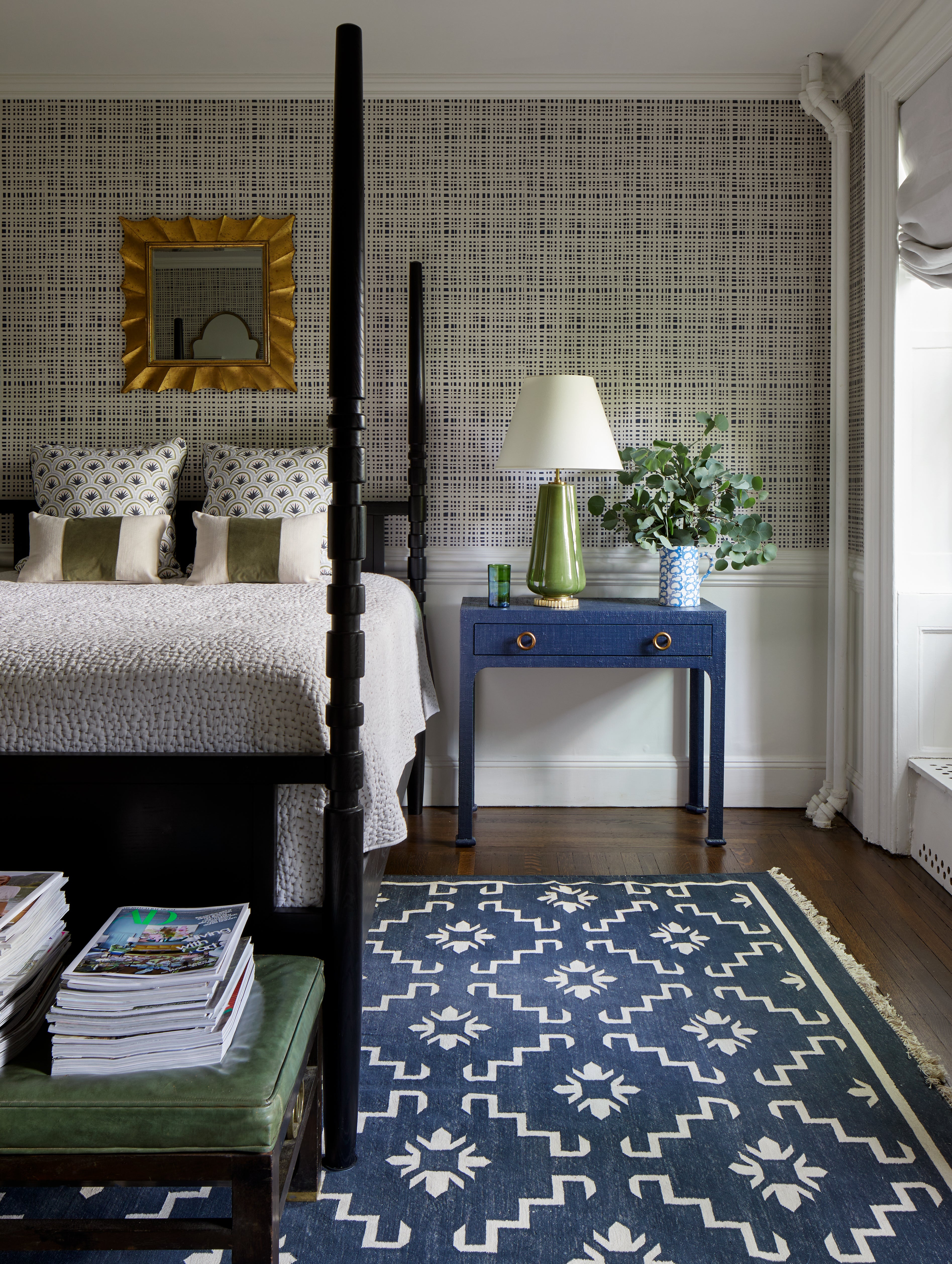 Navy gingham wallpaper in a bedroom with white wainscoting and a black four poster bed styled with white sheets and blue and green art deco custom pillows