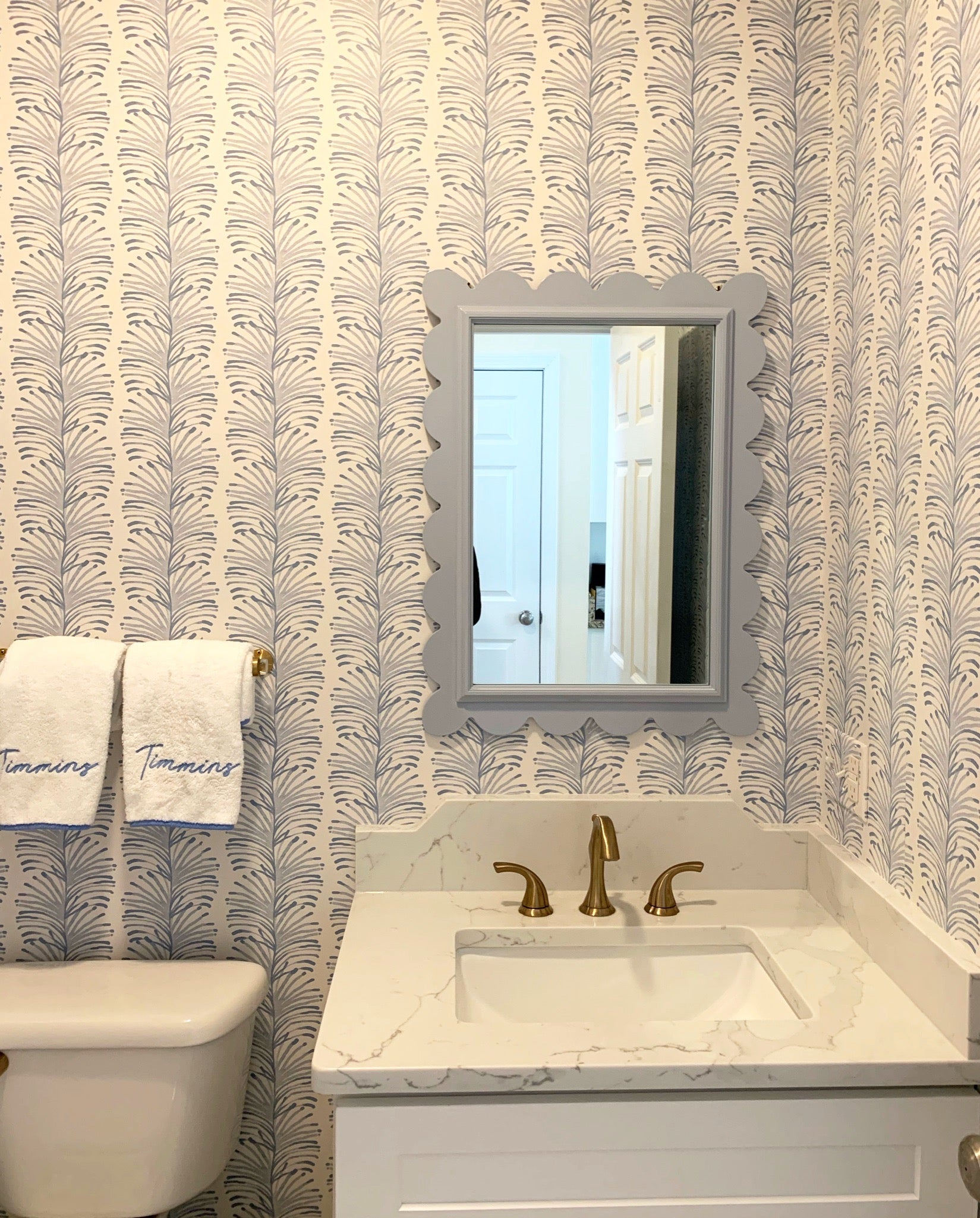 Bathroom with sky blue botanical wallpaper, white vanity and blue scalloped mirror