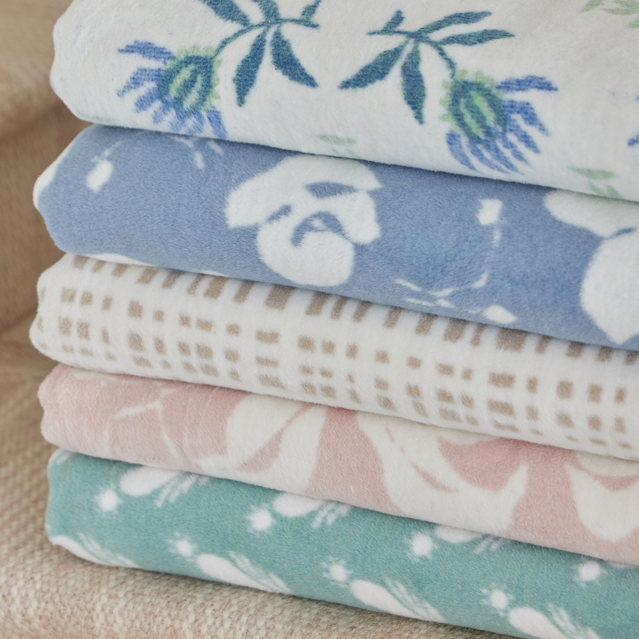 Close up of a stack of 5 patterned blankets on a tan rug