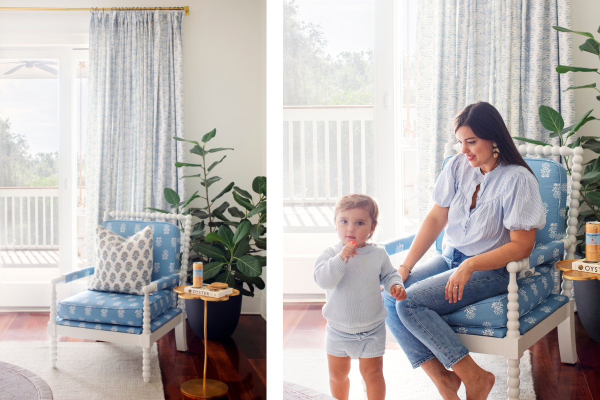 Room corner with blue and white armchair next to a small table with a book and can on top by plants in a big black clay vase next to an illuminated window styled with a Sky Blue Botanical Stripe Custom Curtain on a gold metal rod. Close-up of brunette woman sitting in blue and white armchair by child in front of an illuminated window styled with a Sky Blue Botanical Stripe Custom Curtain