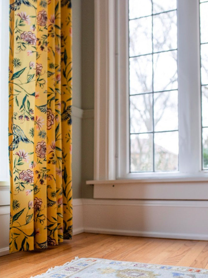 Close up of the bottom of yellow chinoiserie curtains hanging next to a window