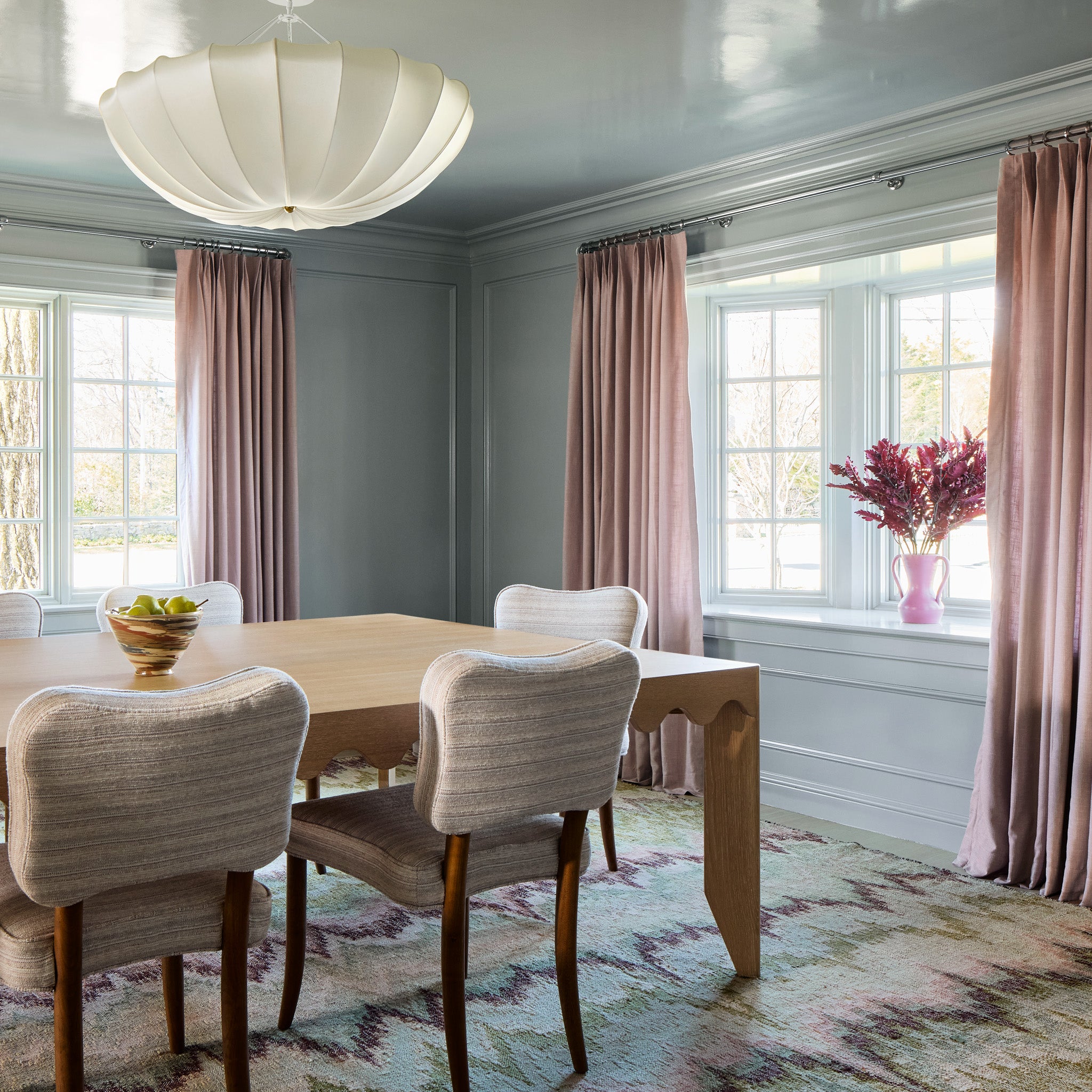 Dining room with pink and green chevron rug and light wooden table and light pink curtains hanging on two windows