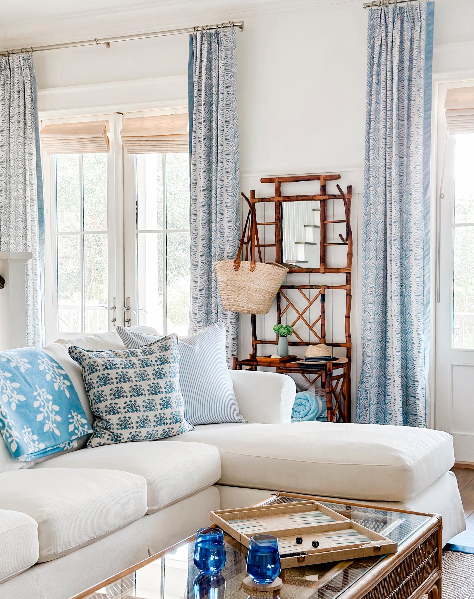 Wooden hanger stand with beach tote bag and hat in between sky blue botanical stripe custom curtains on each side in front of white couch