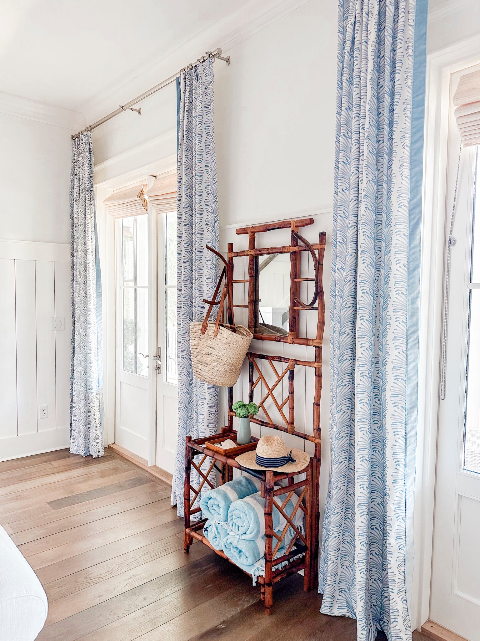 Illuminated entrance styled with Sky Blue Botanical Stripe custom curtains next to a wooden hanger stand with beach hats, totes, and towels