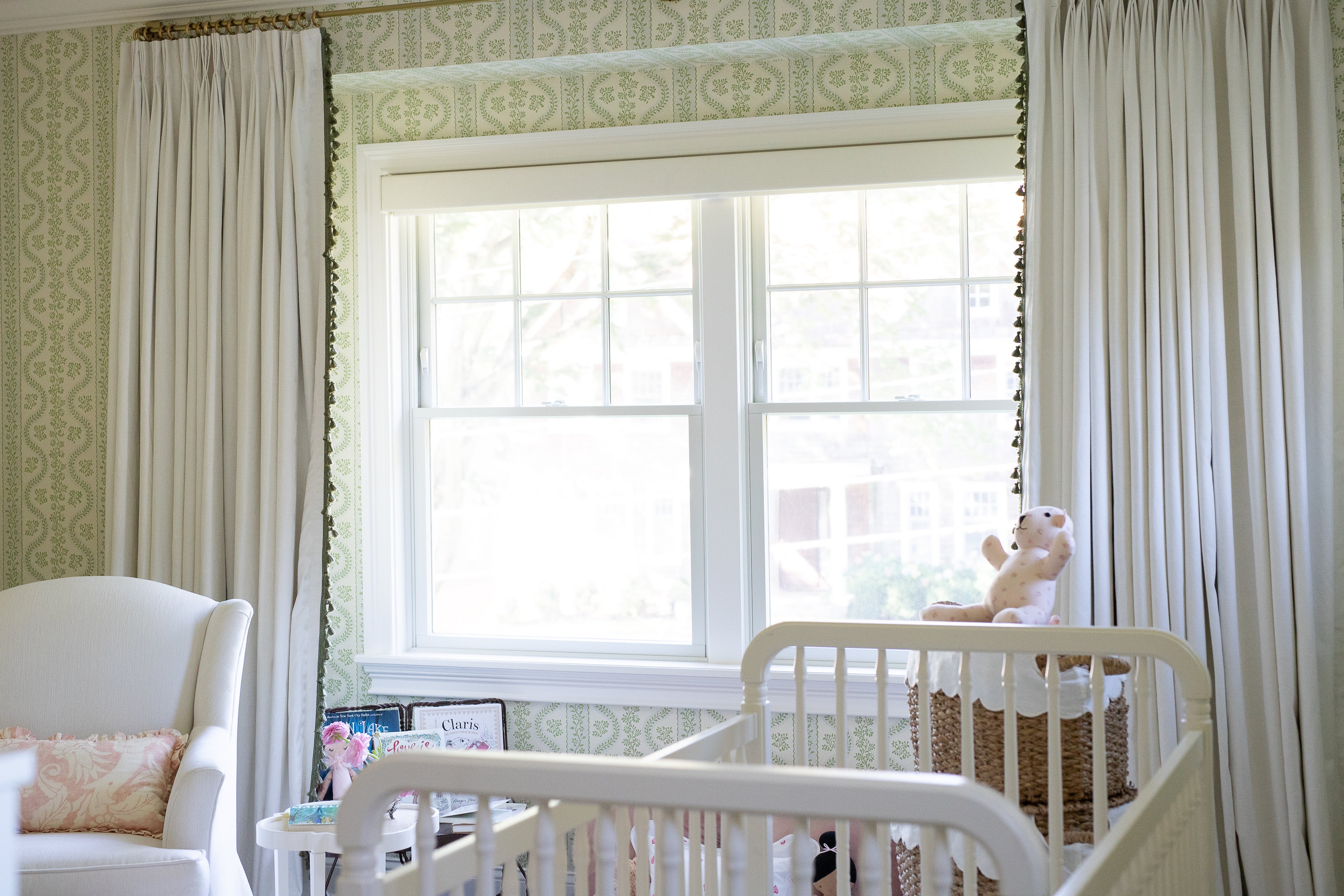 Natural white curtains with sage tassels flanking a window in a nursery with green wallpaper