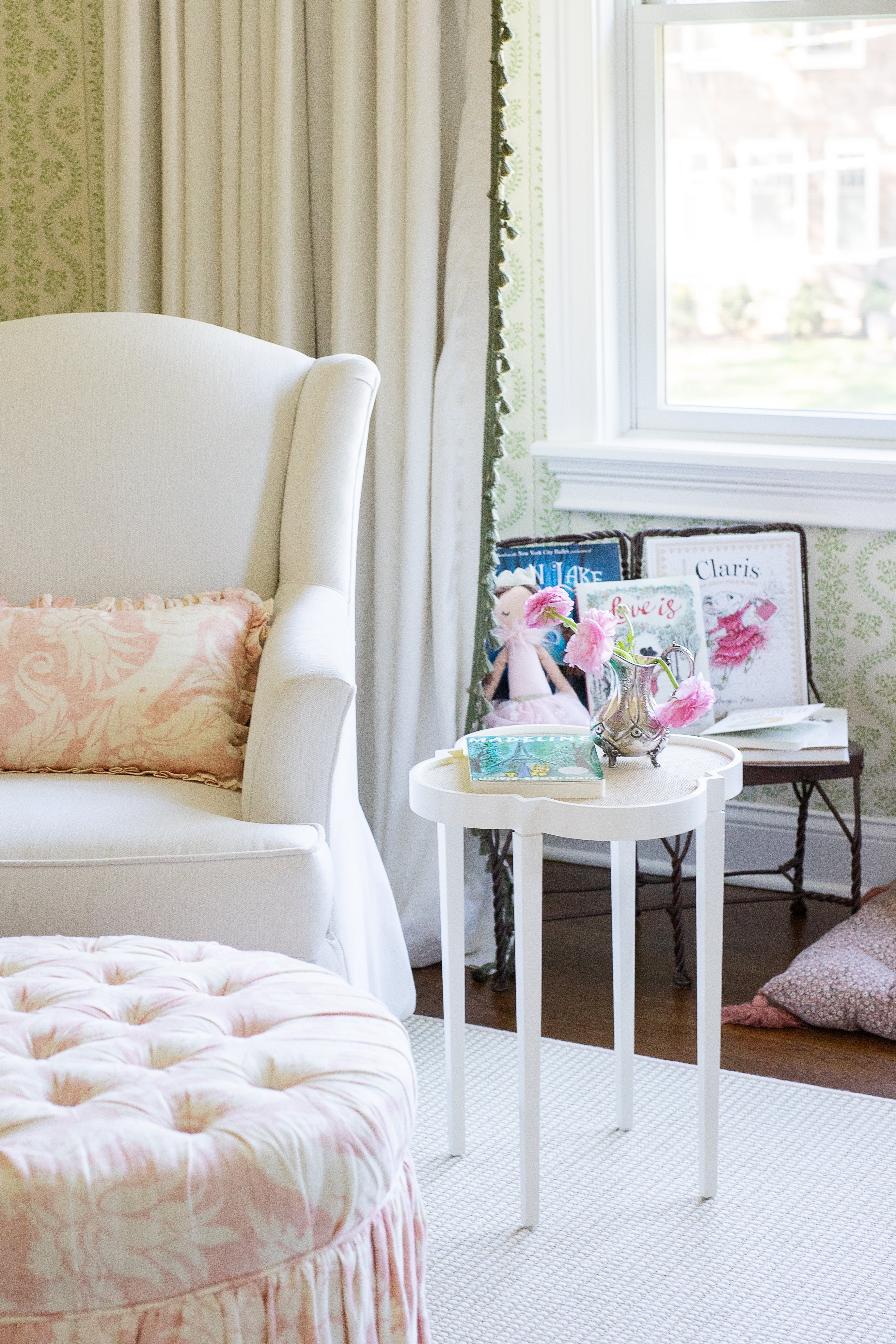 Natural white curtain with green tassel trim hanging behind a white stool and chair with a pink pillow on it