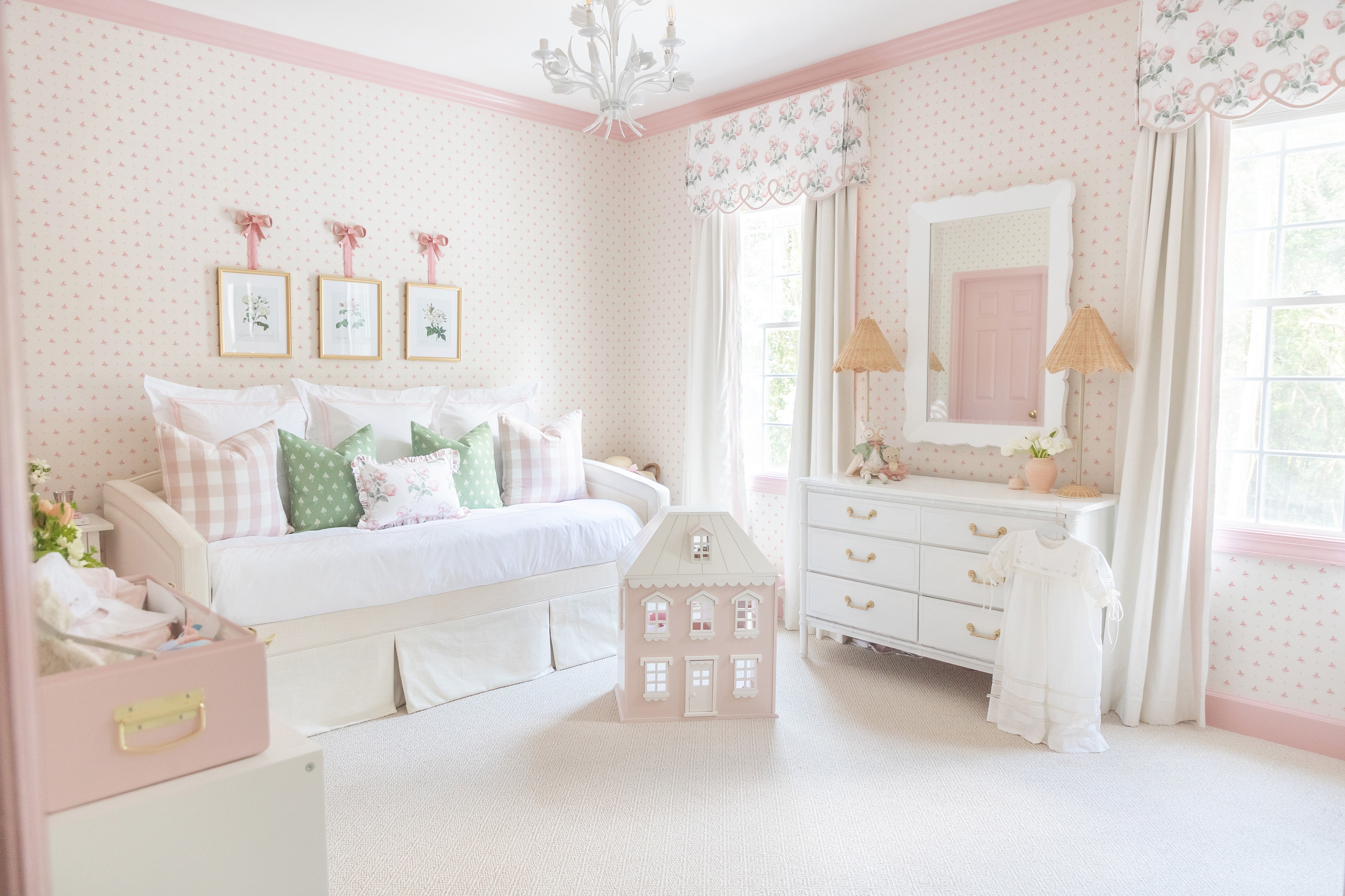 Nursery with pink and white wallpaper and pink painted trim with two windows with natural white curtains and a white daybed with pink and green pillows