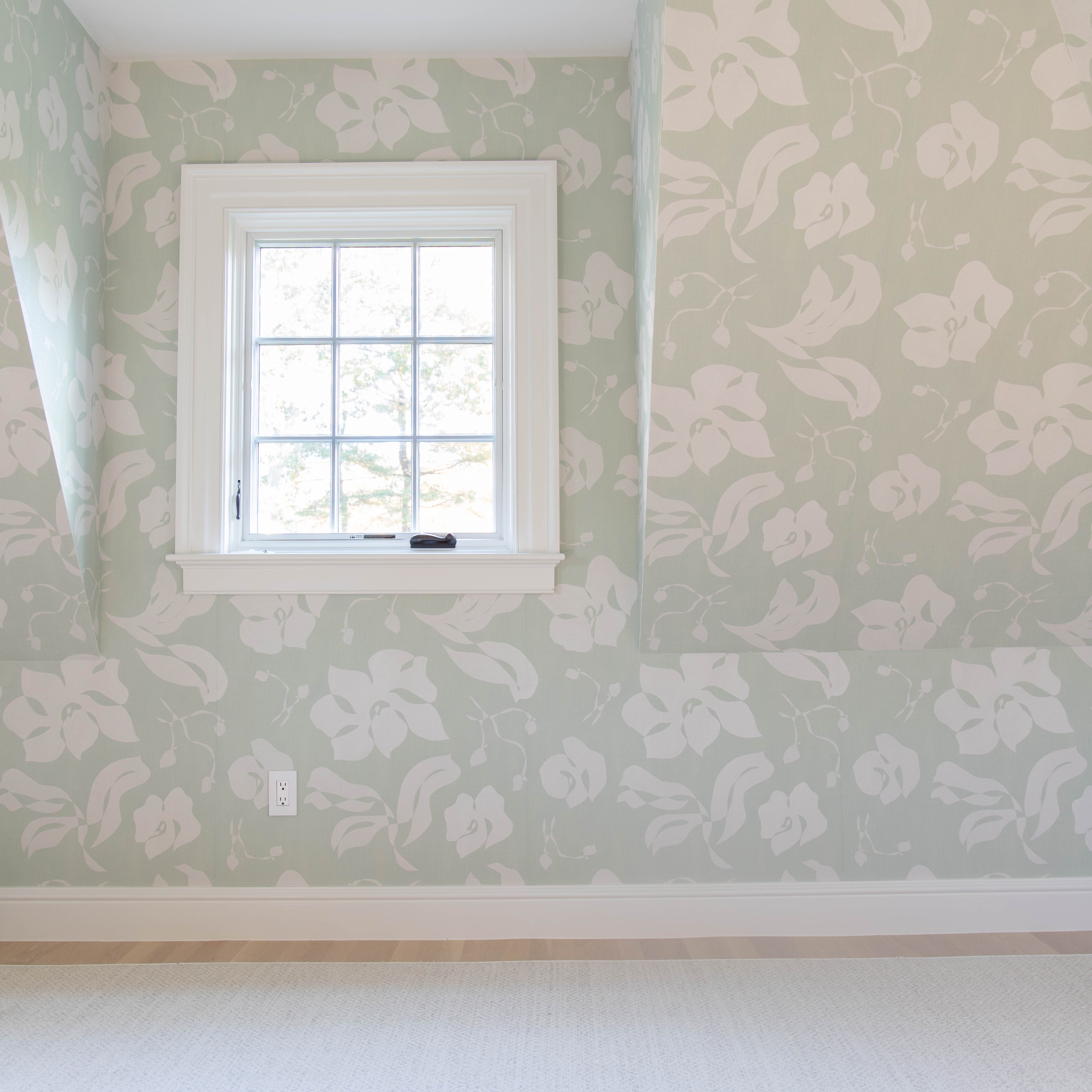 Empty room with mint green floral wallpaper and one window and a cream rug
