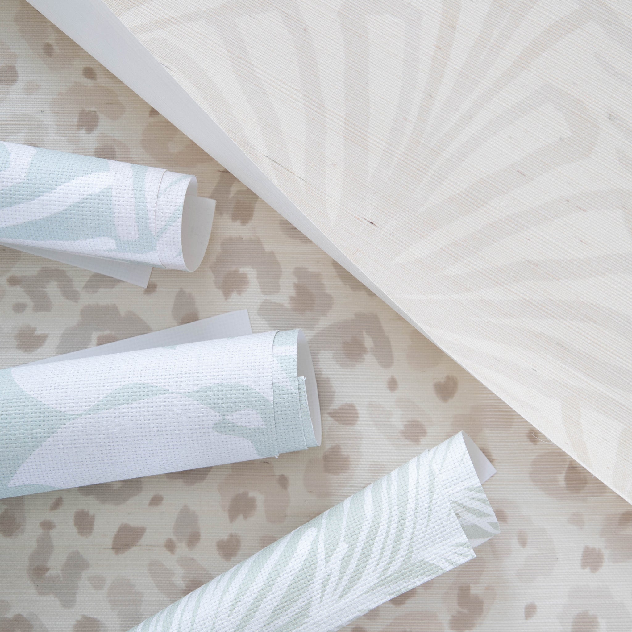 Beige art deco and animal print wallpaper rolls paired with three mint floral wallpaper rolls