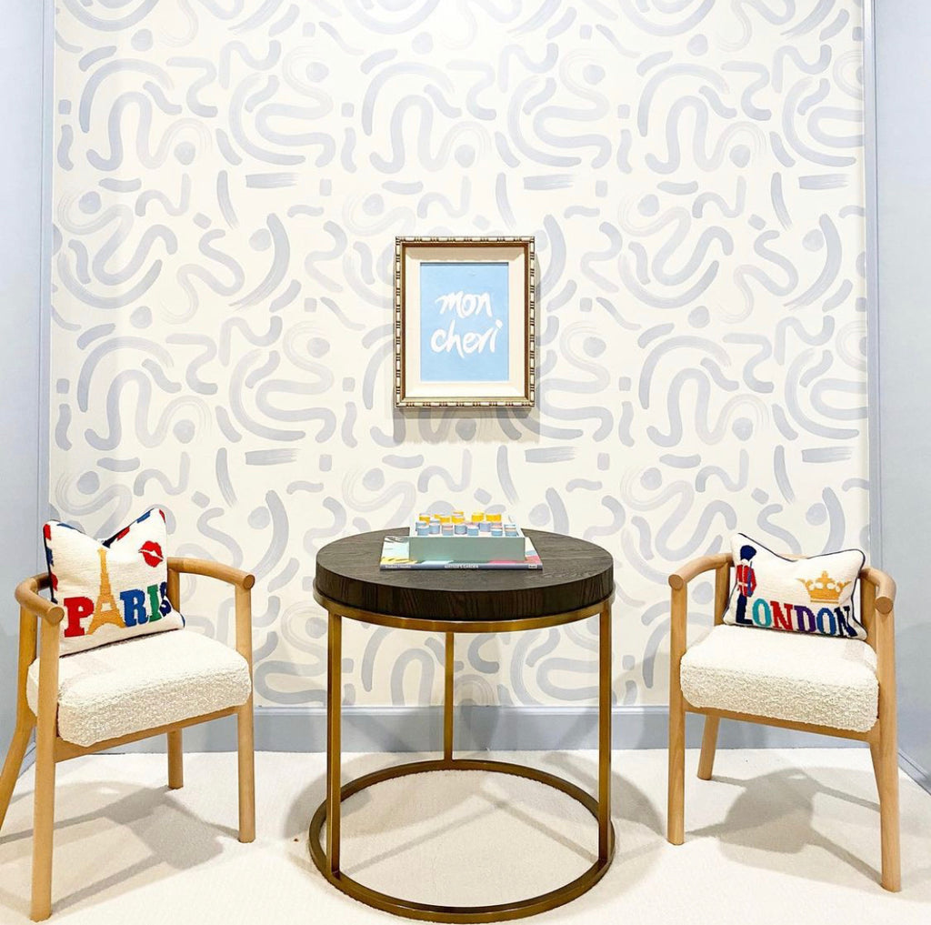 Sky blue abstract wallpaper in a kid's playroom with small white and tan chairs styled with needlepoint pillows