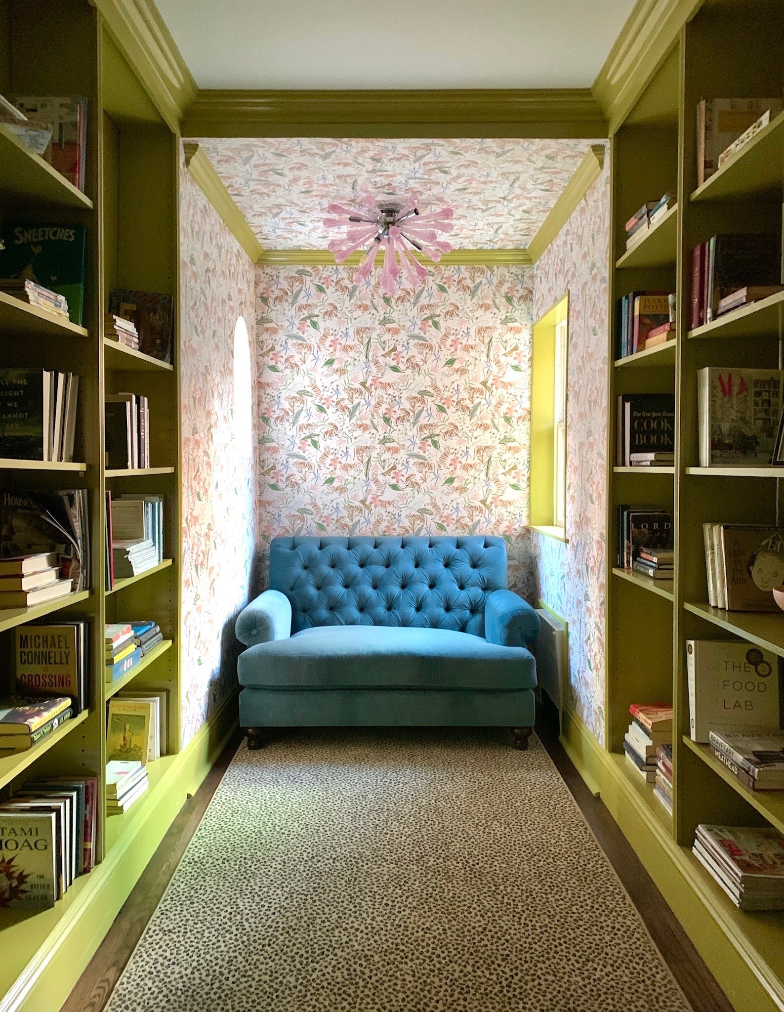 Library with pink chinoiserie wallpaper and chartreuse trim styled with a blue velvet couch